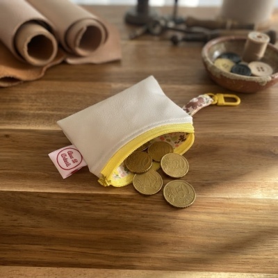 Carteira pequena branca com fecho amarelo e interior floral com moedas de euro sobre mesa de madeira