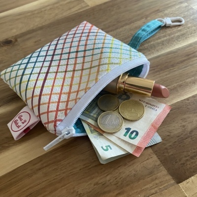 Carteira pequena colorida com fecho, notas de euro, moedas e batom em superfície de madeira