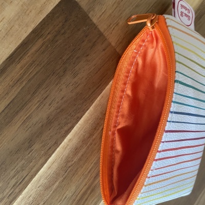 Carteira pequena com fecho de correr laranja e riscas coloridas sobre madeira