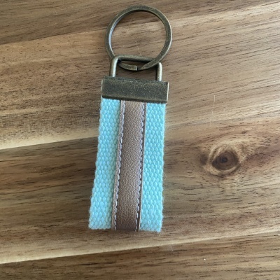 Chaveiro com fita têxtil azul clara e couro castanho sobre madeira clara