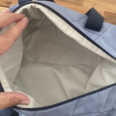 Mochila azul com interior branco e fecho preto aberta, com alça azul escura
