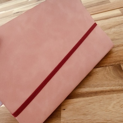 Caderno cor-de-rosa com elástico vermelho sobre mesa de madeira clara