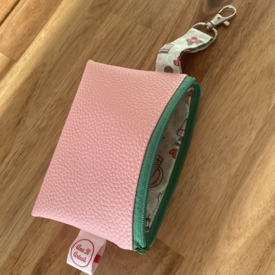 Bolsa pequena rosa com fecho verde e alça estampada com mosquetão sobre superfície de madeira