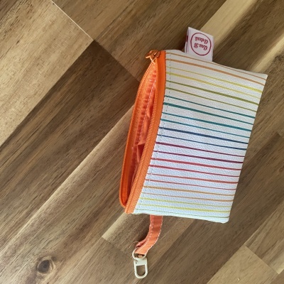 Carteira branca com riscas coloridas e fecho laranja numa mesa de madeira