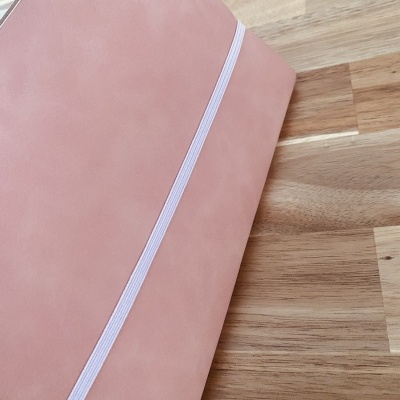 Caderno rosa com elástico branco sobre mesa de madeira clara.