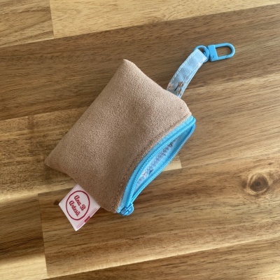 Bolsa pequena bege com fecho e alça azul sobre mesa de madeira