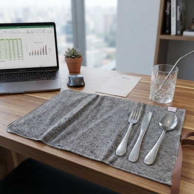 Conjunto de talheres sobre esteira cinza numa mesa com laptop, copo de vidro e mini vaso com planta.