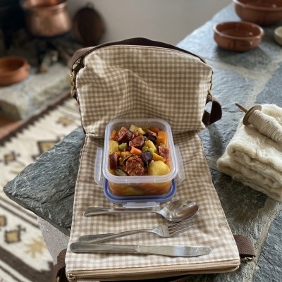 Bolsa térmica xadrez bege com recipiente plástico e talheres sobre mesa de pedra