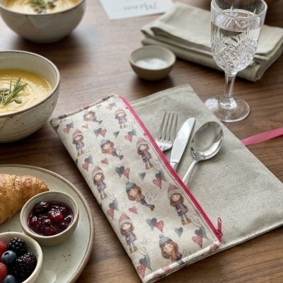 Estojo de tecido com talheres sobre mesa com sopa, croissant e frutas.