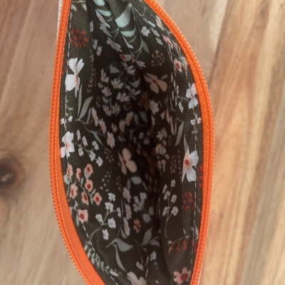 Interior de estojo com zíper laranja e tecido estampado de flores.