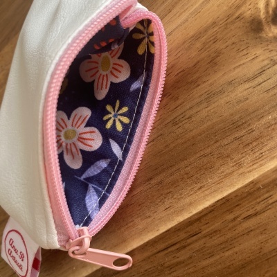Bolsa branca com zíper rosa e interior floral colorido sobre madeira