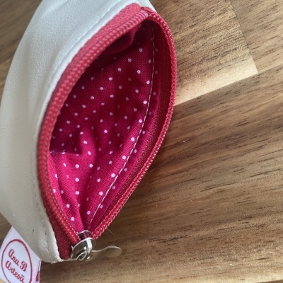 Bolsa branca com fecho vermelho e interior vermelho com bolinhas brancas sobre madeira