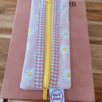 Estojo textil floral com fecho amarelo sobre caderno rosa