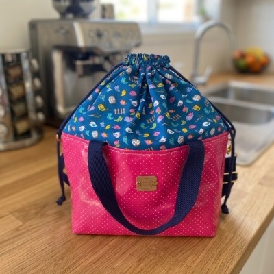 Mala de tecido azul com padrão de pássaros e base rosa com bolinhas brancas numa bancada de cozinha.