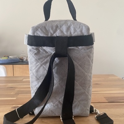 Mochila cinzenta acolchoada com alças pretas sobre mesa de madeira
