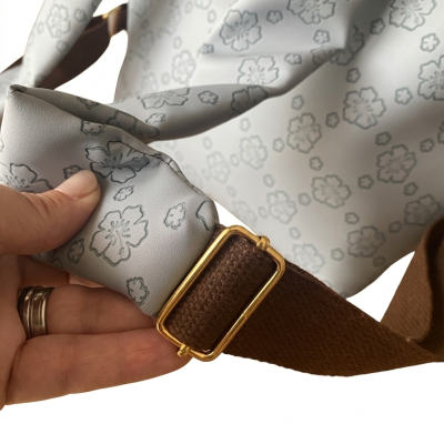 Mala cinza com padrão floral e alça castanha com fivela dourada