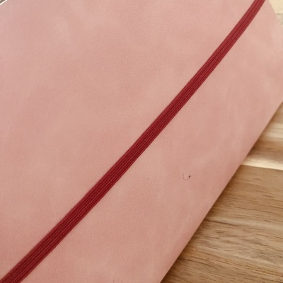 Caderno rosa com elástico vermelho sobre mesa de madeira clara