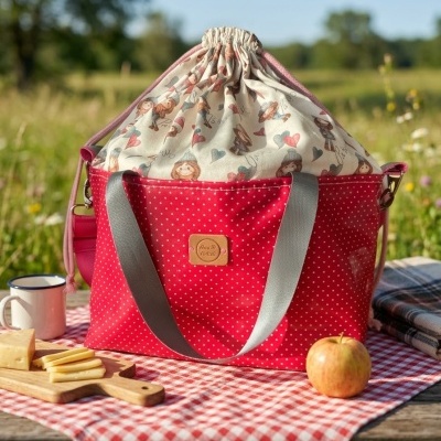 Saco de tecido vermelho com pontos brancos e tecido superior estampado em mesa de piquenique.