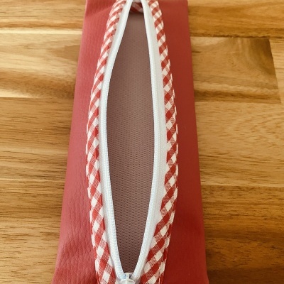 Estojo retangular vermelho com fecho branco e padrão xadrez vermelho e branco.