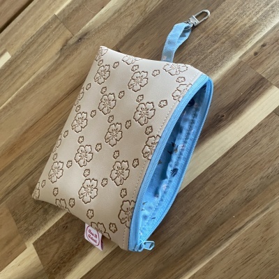 Bolsa pequena creme com padrão floral, fecho azul e interior azul com padrão floral.