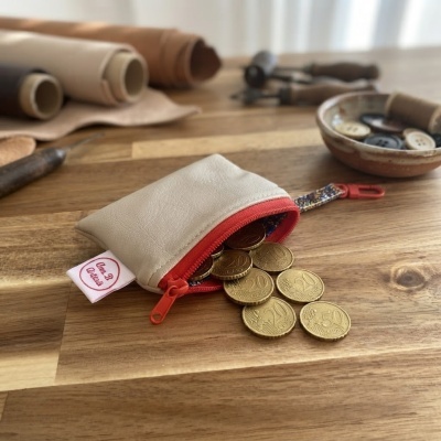 Bolsa pequena de pele sintética bege com fecho vermelho e moedas a sair