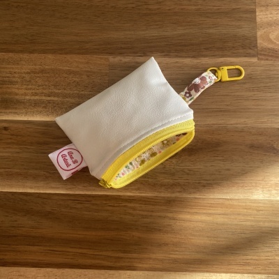 Bolsa pequena branca com fecho amarelo e alça florida sobre mesa de madeira