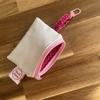 Bolsa pequena branca com interior rosa de bolinhas e fecho de correr rosa em fundo de madeira.