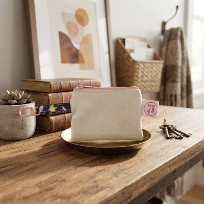 Bolsa pequena branca com fecho rosa e alça azul com padrão floral numa mesa de madeira.