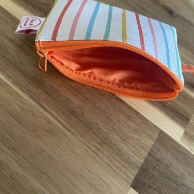 Necessaire branca com riscas coloridas e fecho laranja aberta sobre madeira