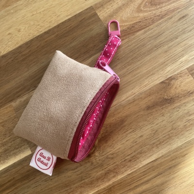 Bolsa pequena bege com alça rosa com pontos brancos e fecho de correr, sobre superfície de madeira.