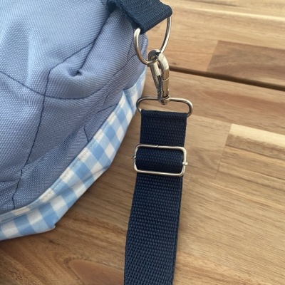 Bolsa azul clara com padrão xadrez azul e branco e alça azul escuro em superfície de madeira