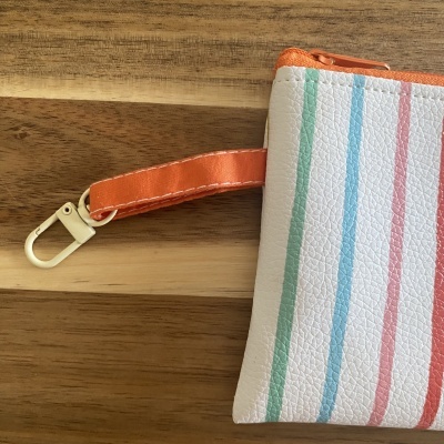 Carteira pequena branca com riscas coloridas, fecho e alça laranja, com mosquetão creme