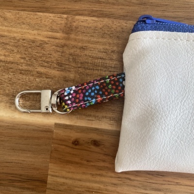 bolsa pequena branca com fecho azul e alça floral colorida sobre madeira