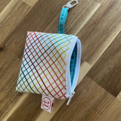 Bolsa pequena branca com linhas coloridas e fecho branco sobre superfície de madeira.