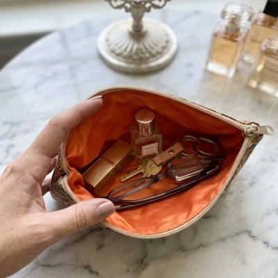 Necessaire aberta com itens pessoais dentro, sobre mesa de mármore com perfumes ao fundo