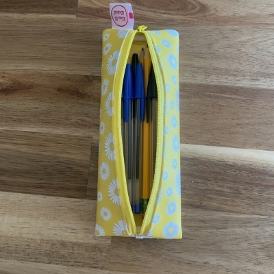 Estojo amarelo com flores brancas e fecho zip aberto mostrando canetas e lápis