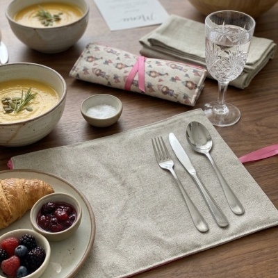 Mesa posta com sopa, croissant, frutas, talheres em tecido de linho e copo de vidro com água.