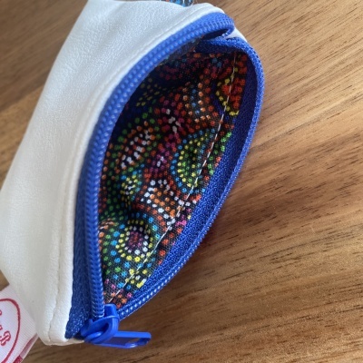 Bolsa pequena branca com interior colorido e fecho azul sobre madeira.