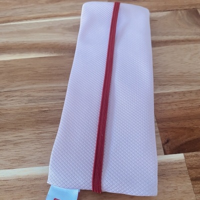 Estojo rosa claro com elástico vermelho e etiqueta branca com ícones sociais