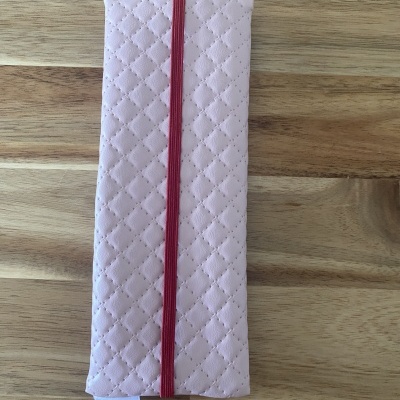 Estojo rosa claro com padrão de losangos e fecho elástico vermelho