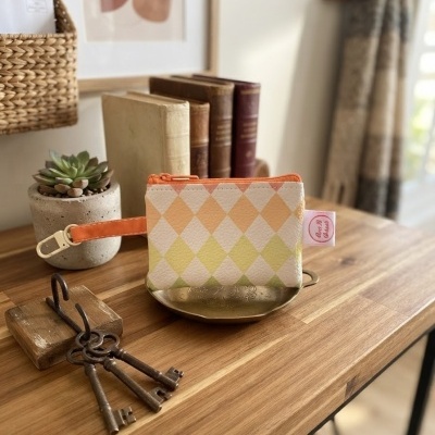 Carteira pequena com padrão de losangos coloridos e fecho laranja numa mesa de madeira com decoração