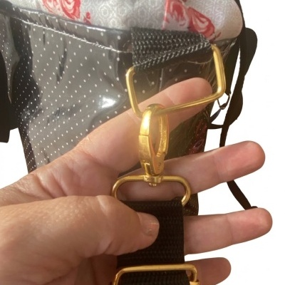 Mão segurando fivela dourada em cinta preta com bolsa preta de pontos brancos e tecido floral.