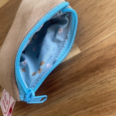 Bolsa pequena bege com fecho azul e interior azul claro com padrão de figuras em madeira.