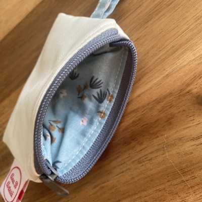 Bolsa pequena branca com fecho zip cinza e interior estampado azul claro sobre madeira