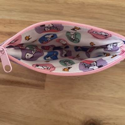Estojo aberto com padrão Snoopy colorido no interior e fecho rosa