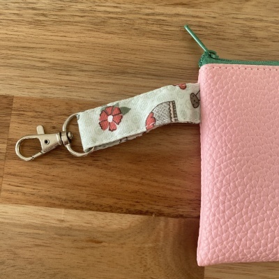 Bolsa rosa com fecho verde e alça estampada com flores, fecho metálico prateado, sobre mesa de madeira.