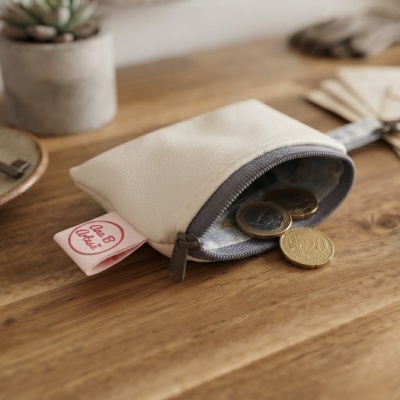 Bolsa pequena de pele sintética cinza clara com moedas e etiqueta rosa sobre mesa de madeira