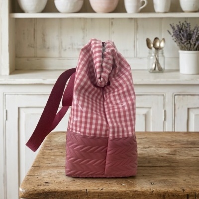 Saco de tecido rosa com padrão de quadrados e base acolchoada sobre mesa de madeira