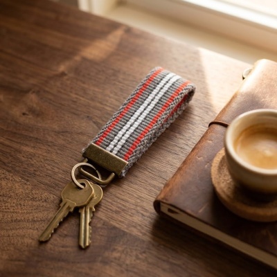 Porta-chaves com riscas vermelhas, brancas e cinzentas numa mesa de madeira junto a um caderno castanho e um café.