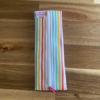 Estojo listrado em tecido com fecho zip cor-de-rosa sobre mesa de madeira.